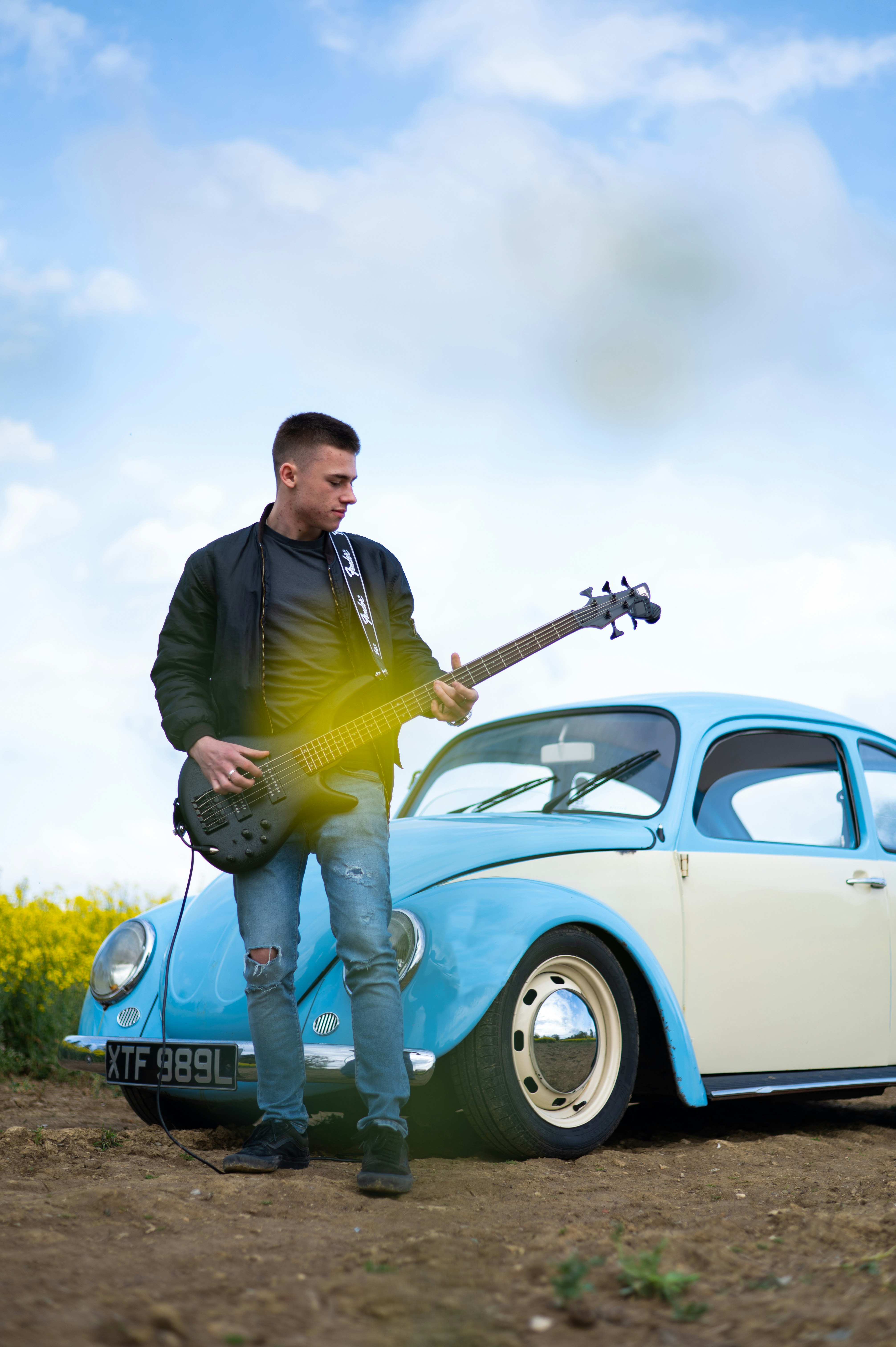 man in black jacket and yellow pants standing beside blue volkswagen beetle